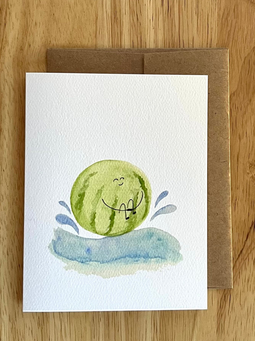 Whimsical watercolor illustration of a round watermelon splashing into blue water with water droplets flying.