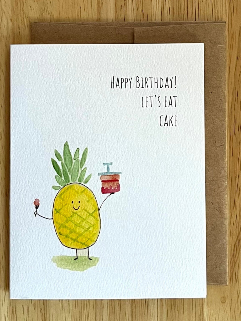 Watercolor pineapple character holding a slice of cake with a cherry on top and the text 'Happy Birthday! Let's Eat Cake'.