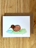 Mei Pie Studio Greeting card with a watercolor illustration of a kiwi bird on a wooden surface