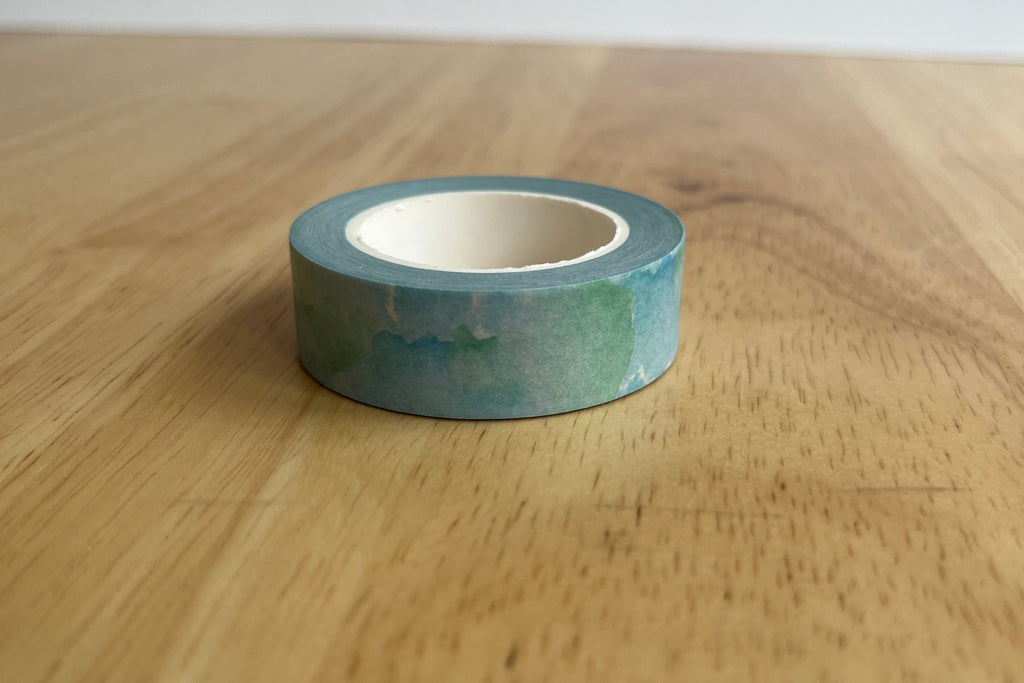 Roll of green washi tape on a wooden surface with a white background