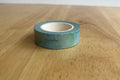 Roll of green washi tape on a wooden surface with a white background