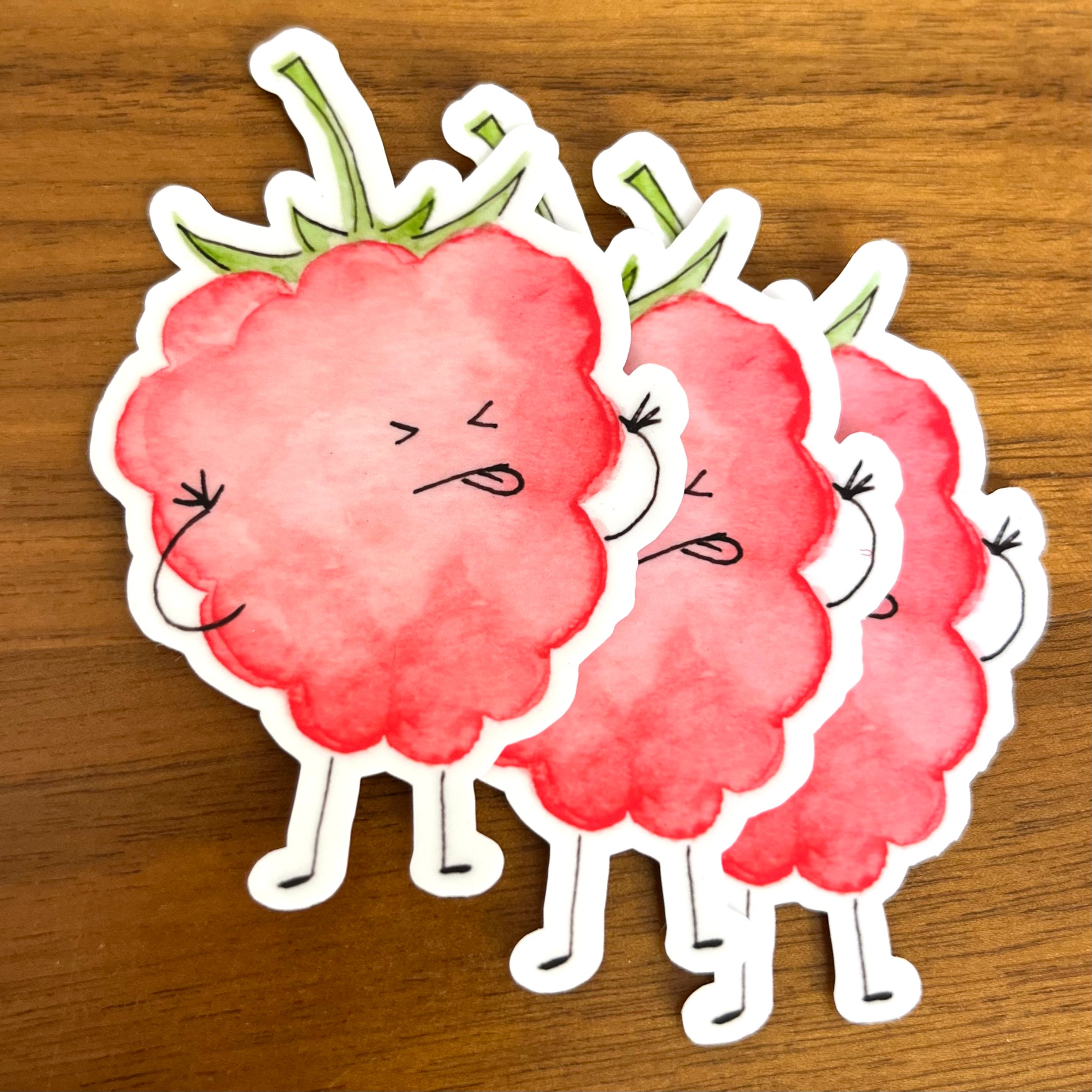 Three cartoon raspberry stickers with a watercolor pink-red body, green stems, and simple facial expressions arranged on a wooden surface.