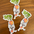 Three die-cut stickers featuring cute illustrated carrots in white karate uniforms with green leafy tops, placed on a brown wooden surface.