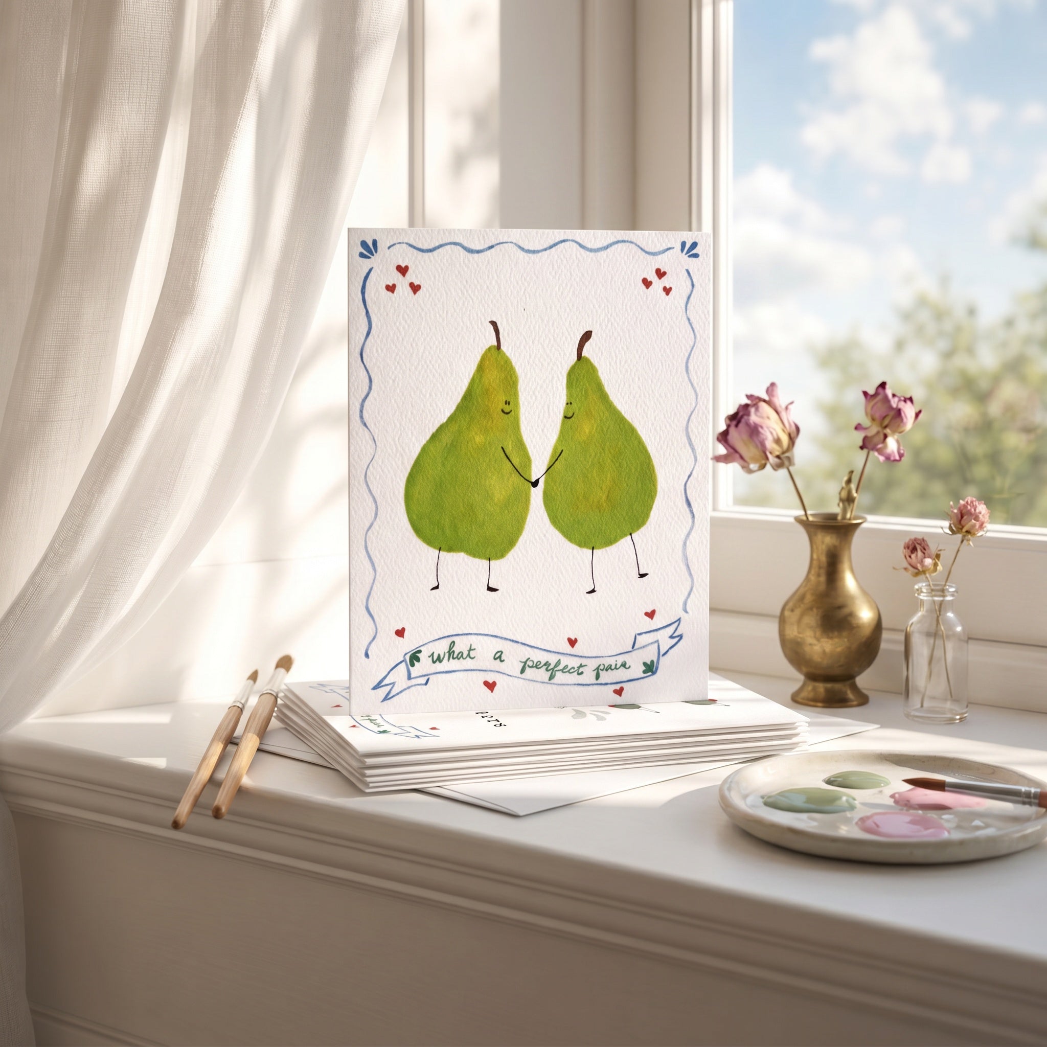 Two pears holding hands with a banner below on a windowsill with art supplies.