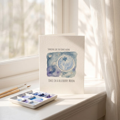 Card with watercolor design of a moon and stars on a windowsill with art supplies.