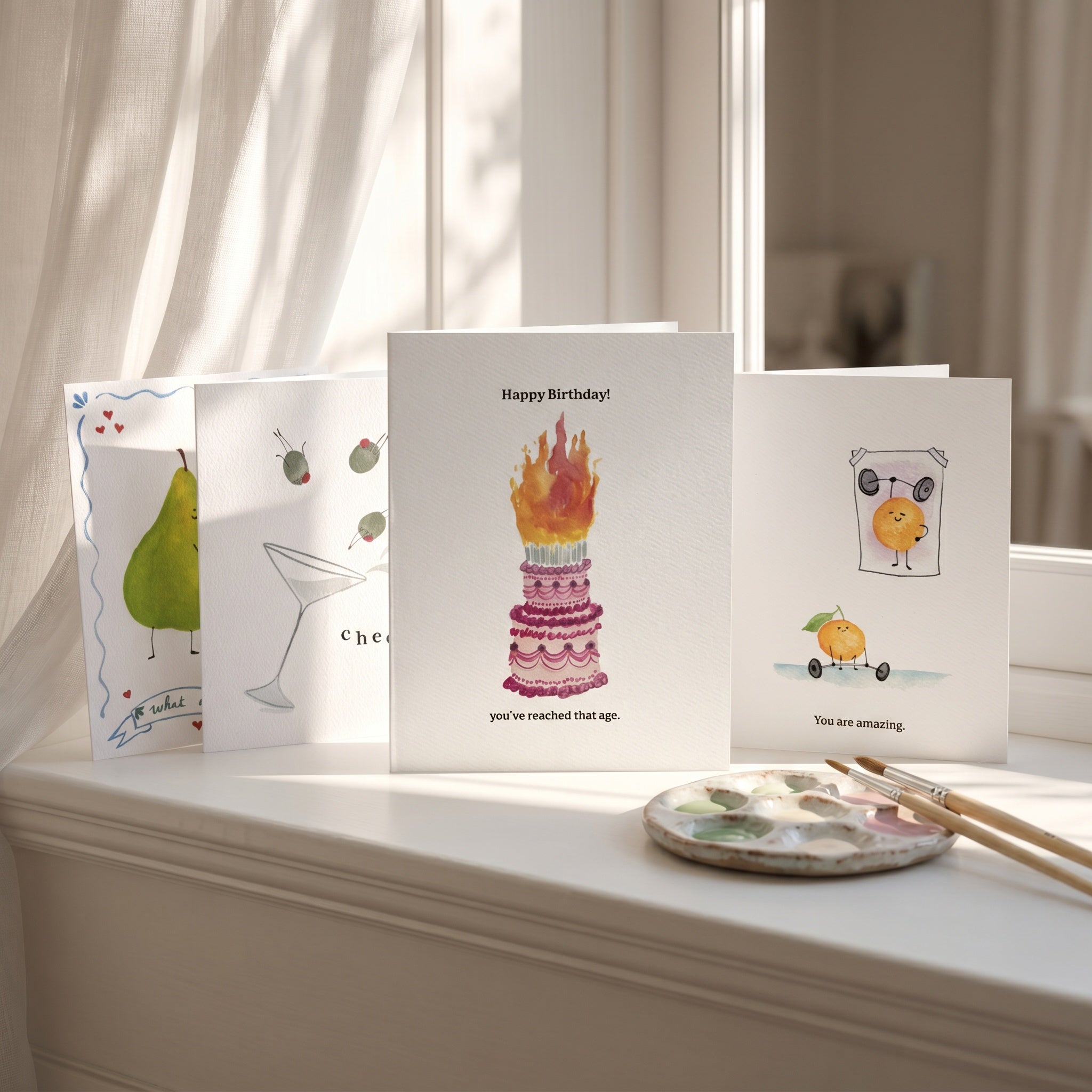 Set of greeting cards on a windowsill with a paint palette and brushes.