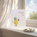 Birthday card with a pineapple illustration on a windowsill with a scenic view.