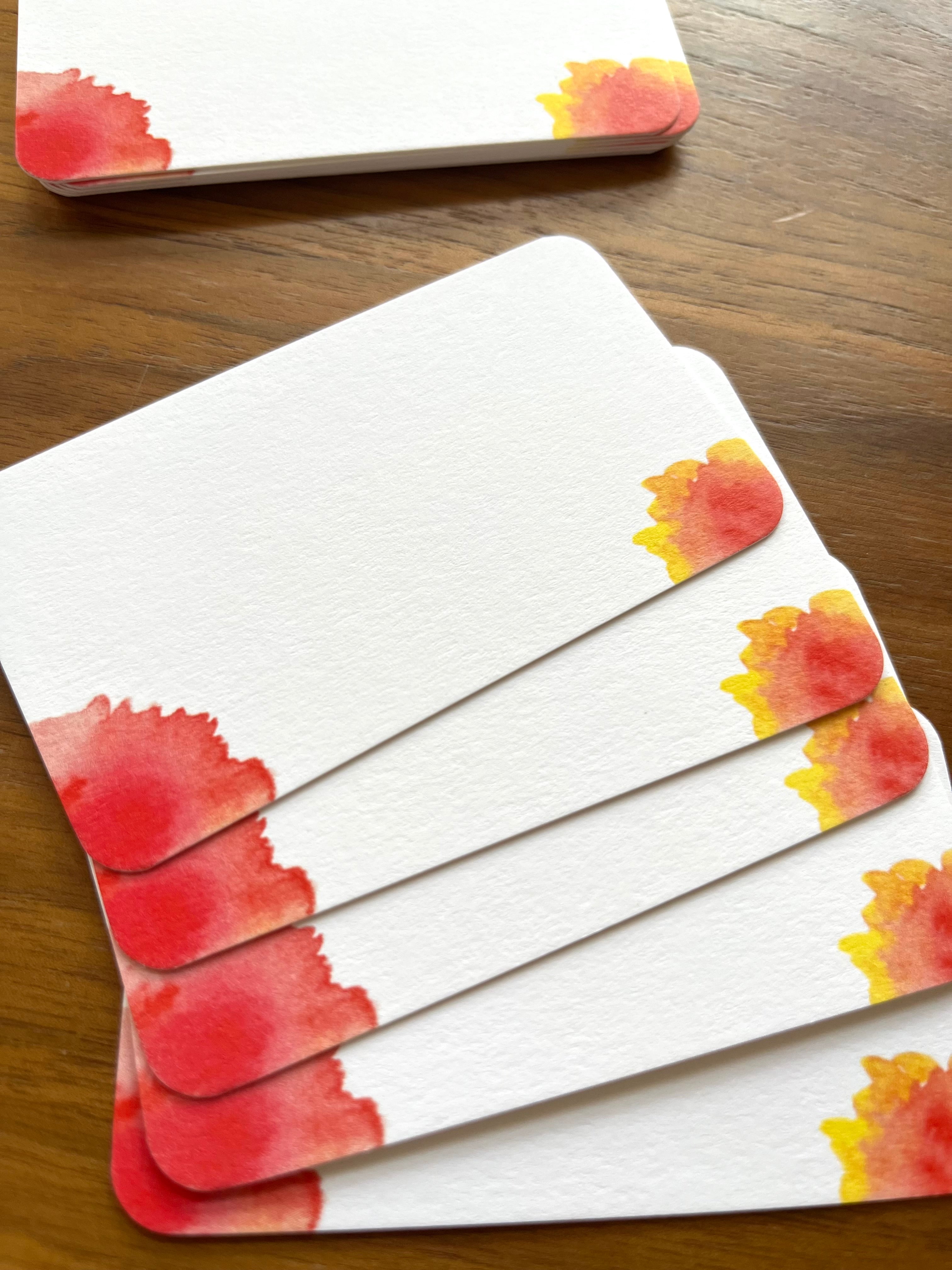 mei pie studio minimalist water color orange, red and yellow sunburst mini note set  on classic crest neenah stock. close up on a wooden table