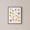 A framed watercolor art print of cute, colorful cartoon fruits hanging on a textured beige wall above a light wood console table with a ceramic vase of dried grass.